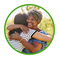 Older, attractive Black lady with eyes closed and big smile hugging closely teenage daughter.